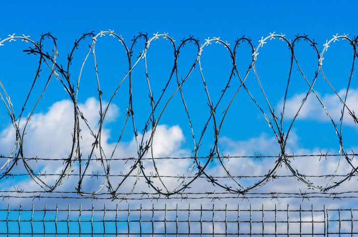 fence with barbed wire against blue sky with clouds, security concept