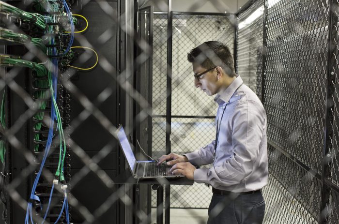 Hispanic man technician doing diagnostic tests on computer servers in a large server farm.