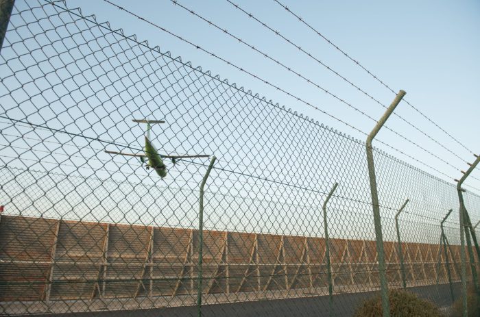 Modern aircraft flying against cloudless blue sky behind security fence in airport